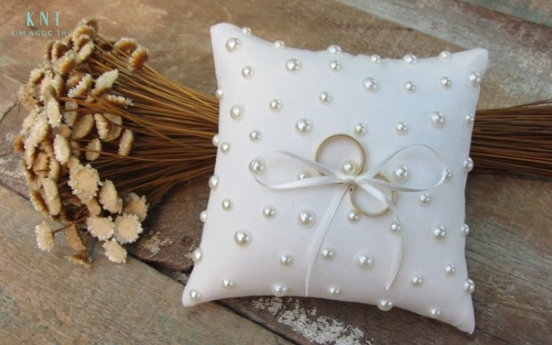 Gối nhẫn cưới nhỏ gọn, đính ngọc trai và ruy băng, dùng để đặt và giữ cặp nhẫn trong suốt nghi thức trao nhẫn