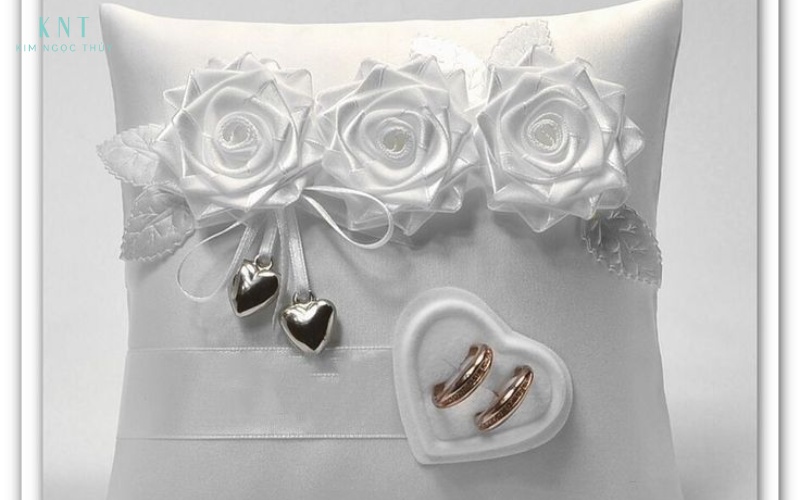 Gối nhẫn satin trắng trang trí hoa lụa tôn vẻ ấm áp và hài hòa cho cặp nhẫn vàng trong nghi thức trao nhẫn